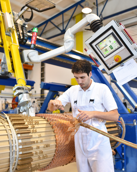 Factory worker winding copper coils on industrial machinery with a control panel
