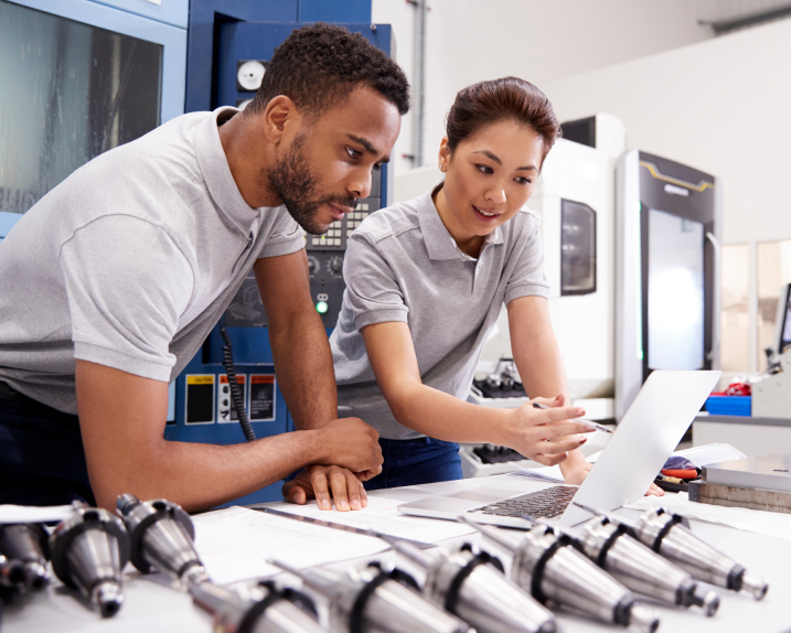 Manufacturing team reviewing production plans on a laptop beside machined parts