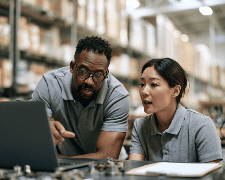 Coworkers in distribution warehouse discussing something on laptop