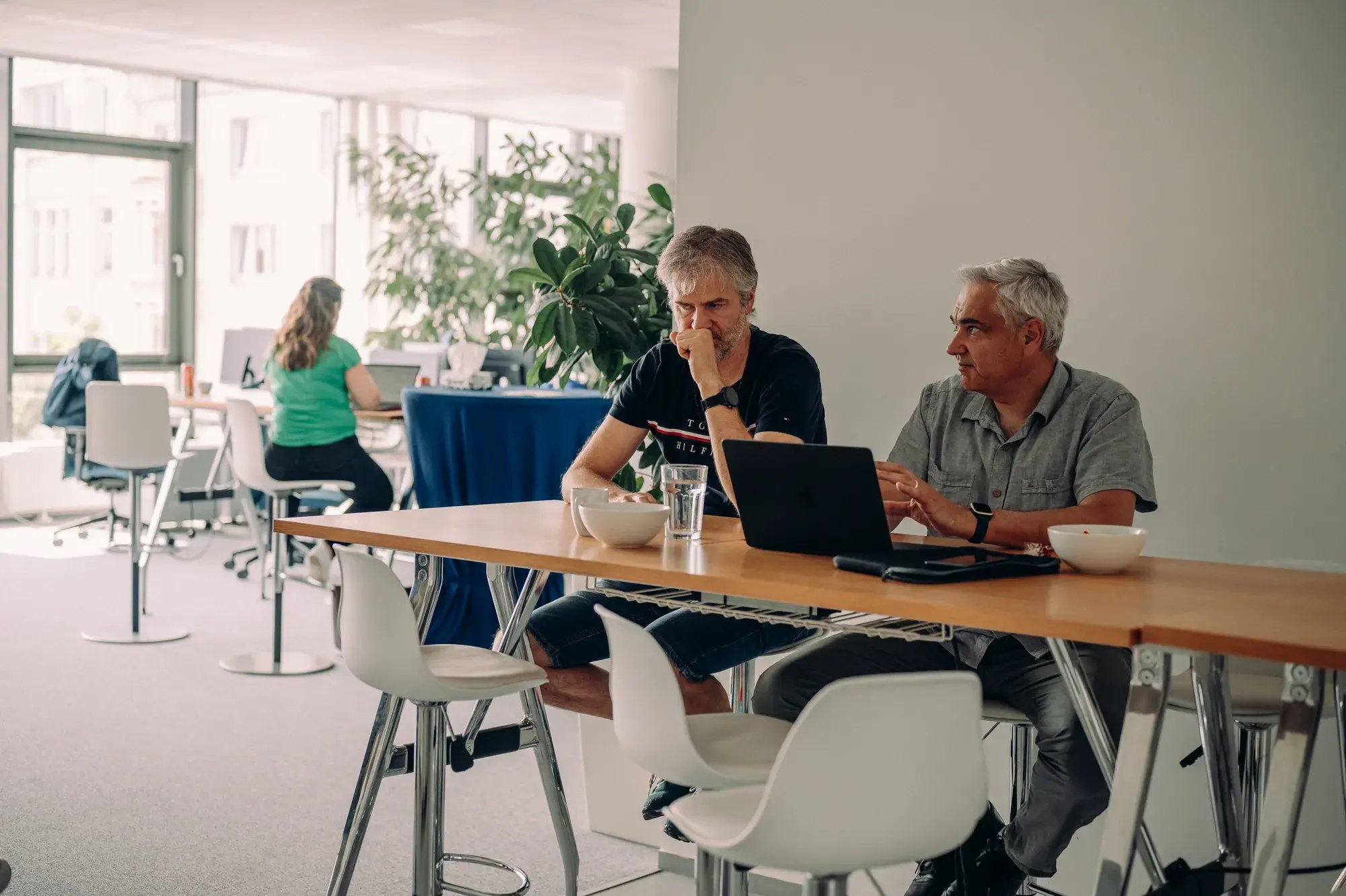 Two Pricefx team members discussing work in the Prague office with colleagues behind them