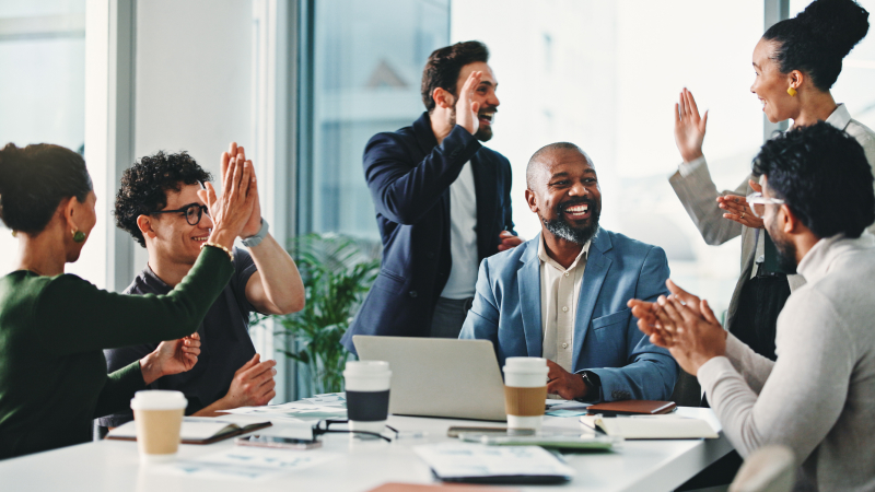 Team celebrating in meeting with high fives around a laptop