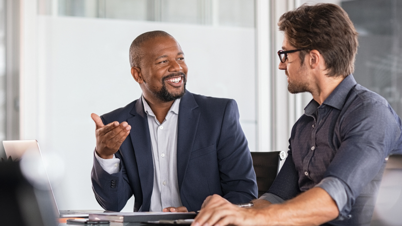 Two colleagues in an office discussing work at a conference table