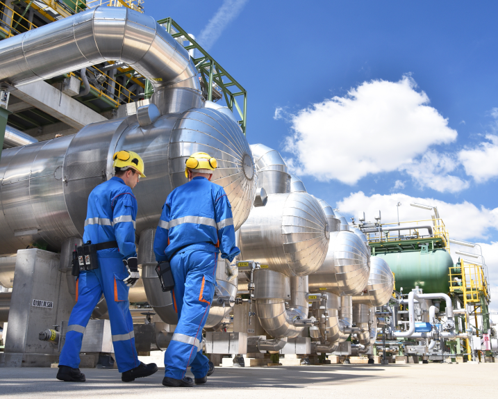 Two workers inspect industrial piping and equipment at a processing plant