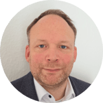 Dr. Jan Wieneke smiling in front of the white wall wearing shirt.