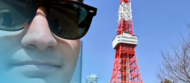 Close-up of a person in sunglasses beside a red-and-white tower under a clear blue sky