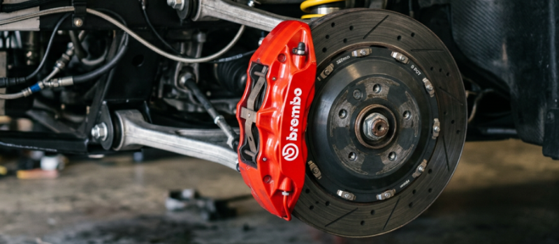 Close-up of car brake disc, red caliper, and suspension components