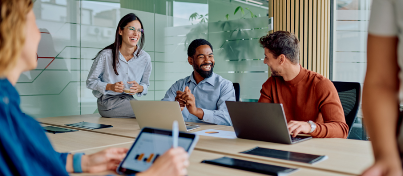 Colleagues smiling during a meeting around laptops in a glass-walled office