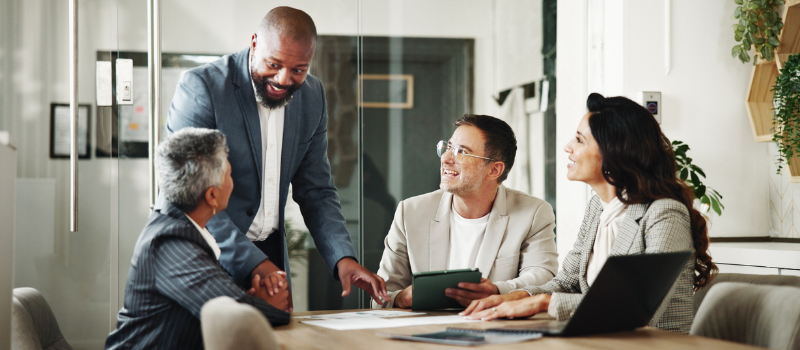 Four colleagues in a meeting room discussing documents around a conference table