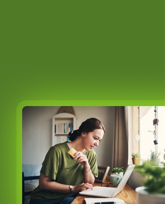 Person holding a payment card while using a laptop at home