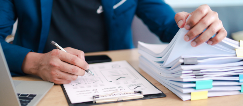 Person reviewing printed reports and flipping through paperwork at desk