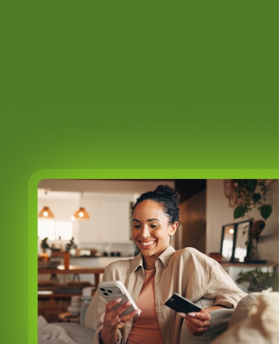 Person shopping online on a smartphone while holding a credit card at home
