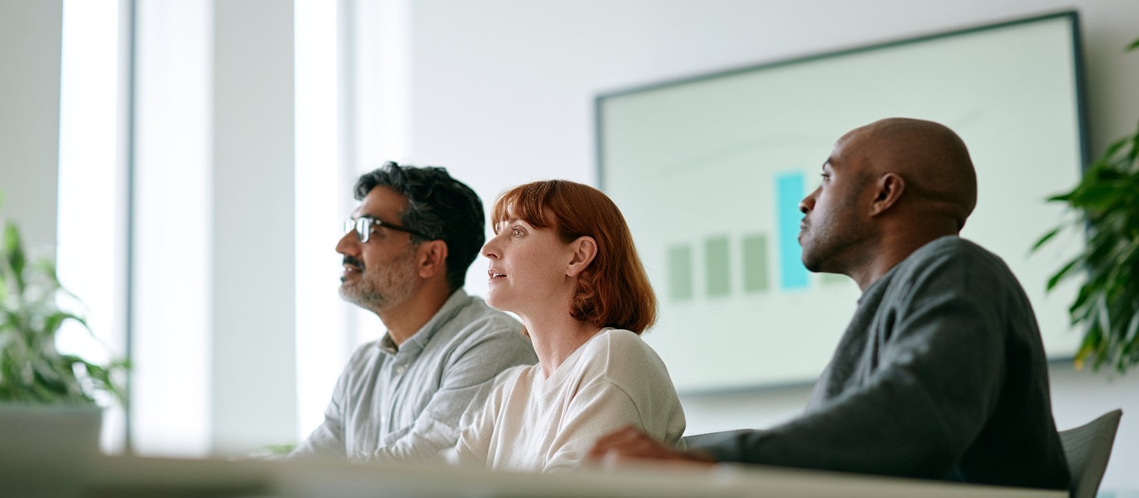 Three colleagues watch a presentation screen during a results review