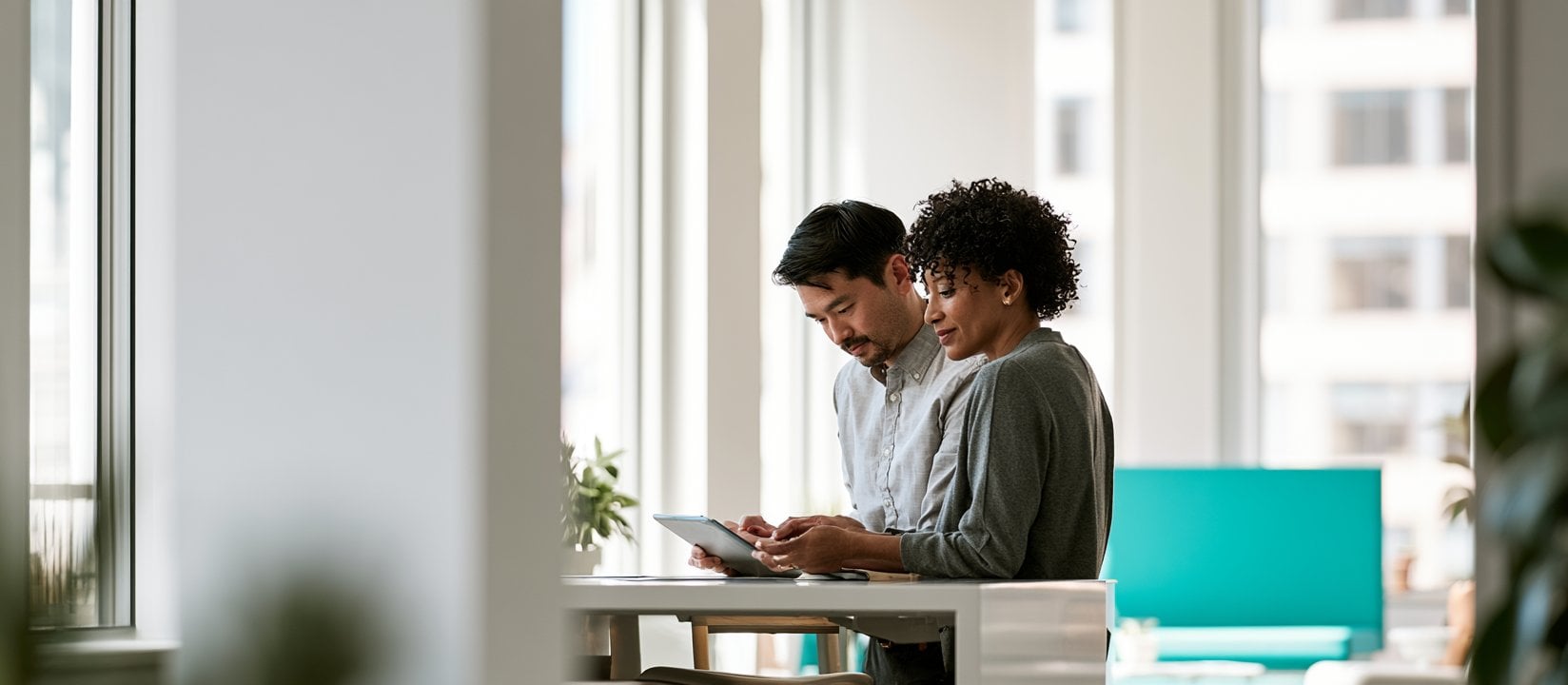 Two coworkers review a tablet together at a standing desk in a bright office-1