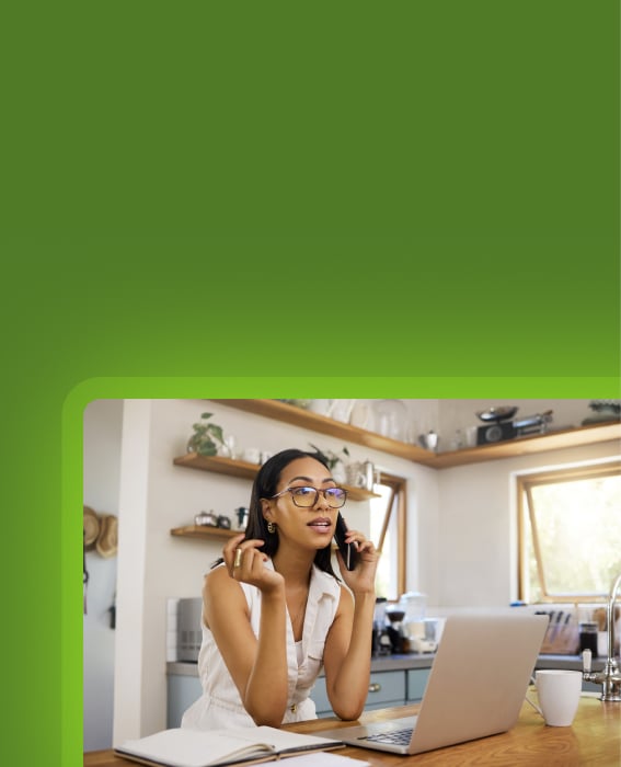 Professional on a phone call beside a laptop and notebook in a home office