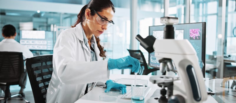 Scientist uses pipette at lab workstation beside a microscope