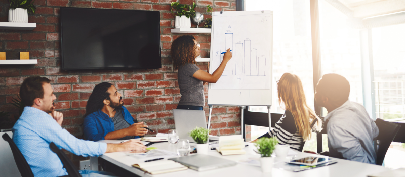 Team watches presenter explain a bar chart in a meeting room
