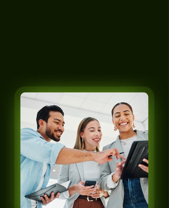 Three colleagues smiling and reviewing content on a tablet in the office