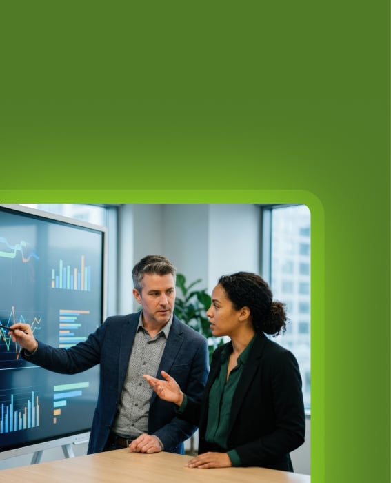Two colleagues review charts on a large display during a business discussion