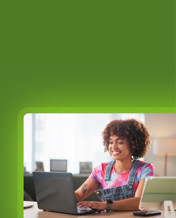 Woman smiling while working on a laptop at home with a tablet nearby