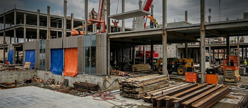 Workers installing concrete panels and steel framing at a multistory construction site